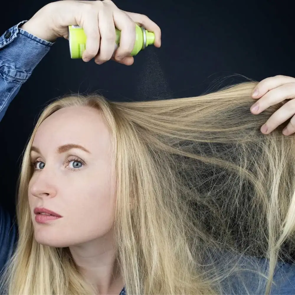 A woman joyously spraying the best dry shampoo onto her lush extensions