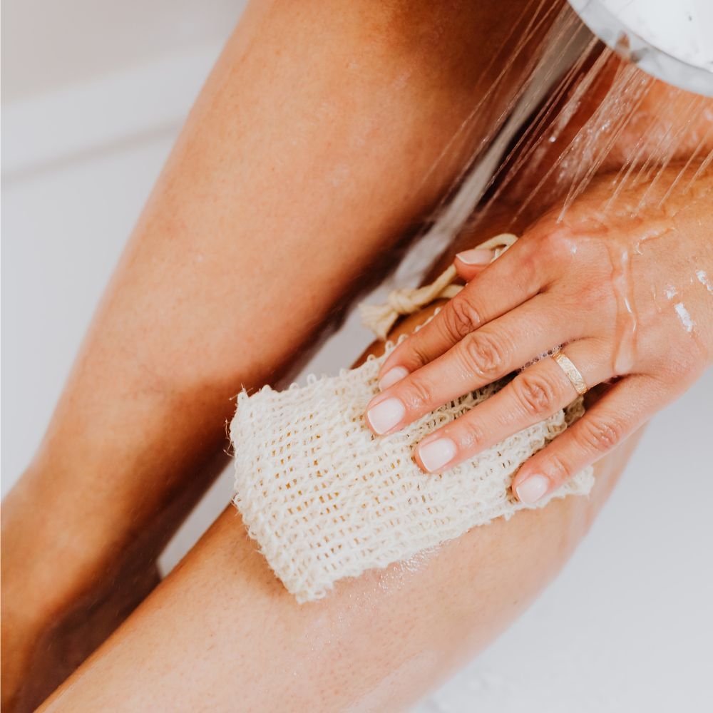 applying body wash on legs using a loofah