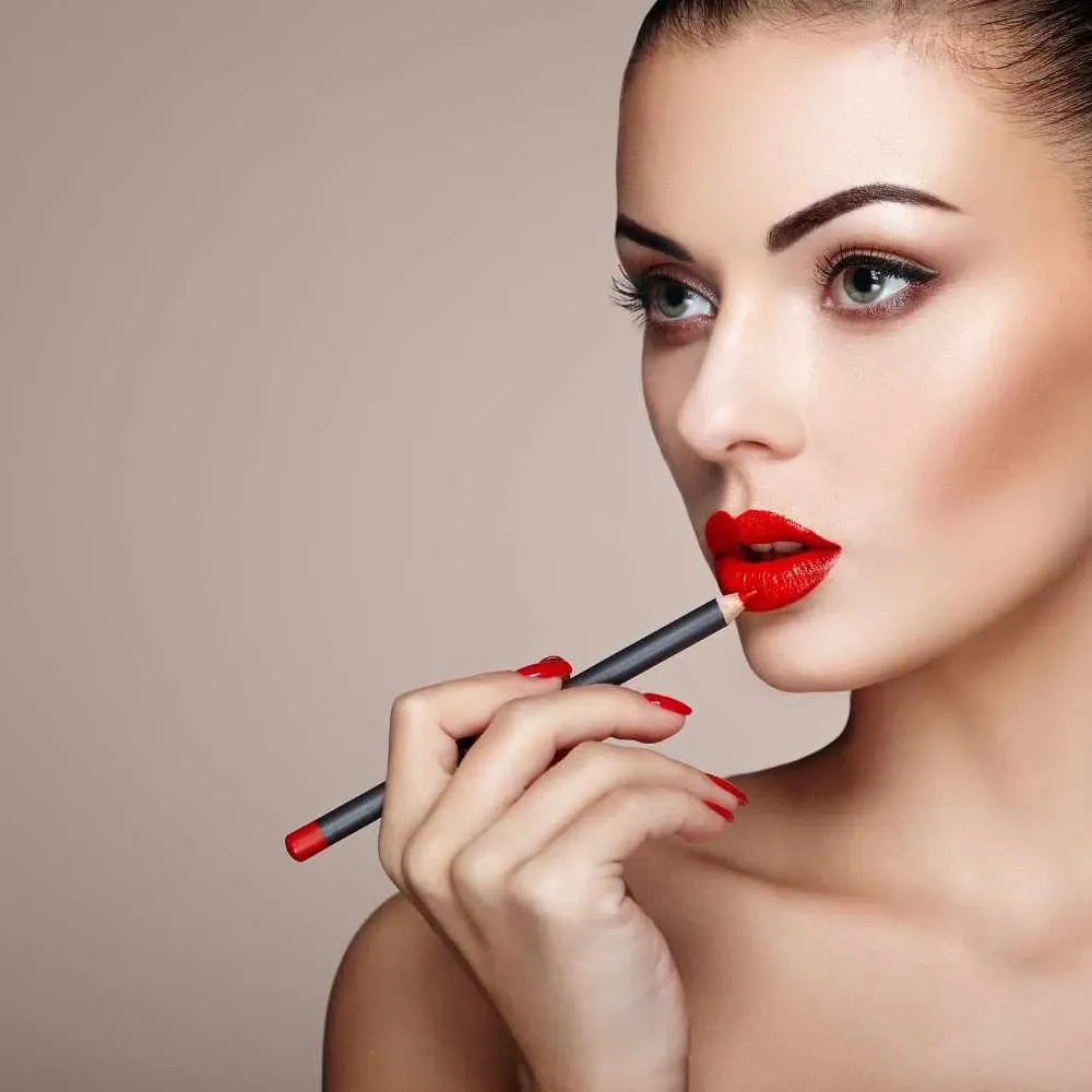 woman with bright red lips and red nails applying bright red lipliner