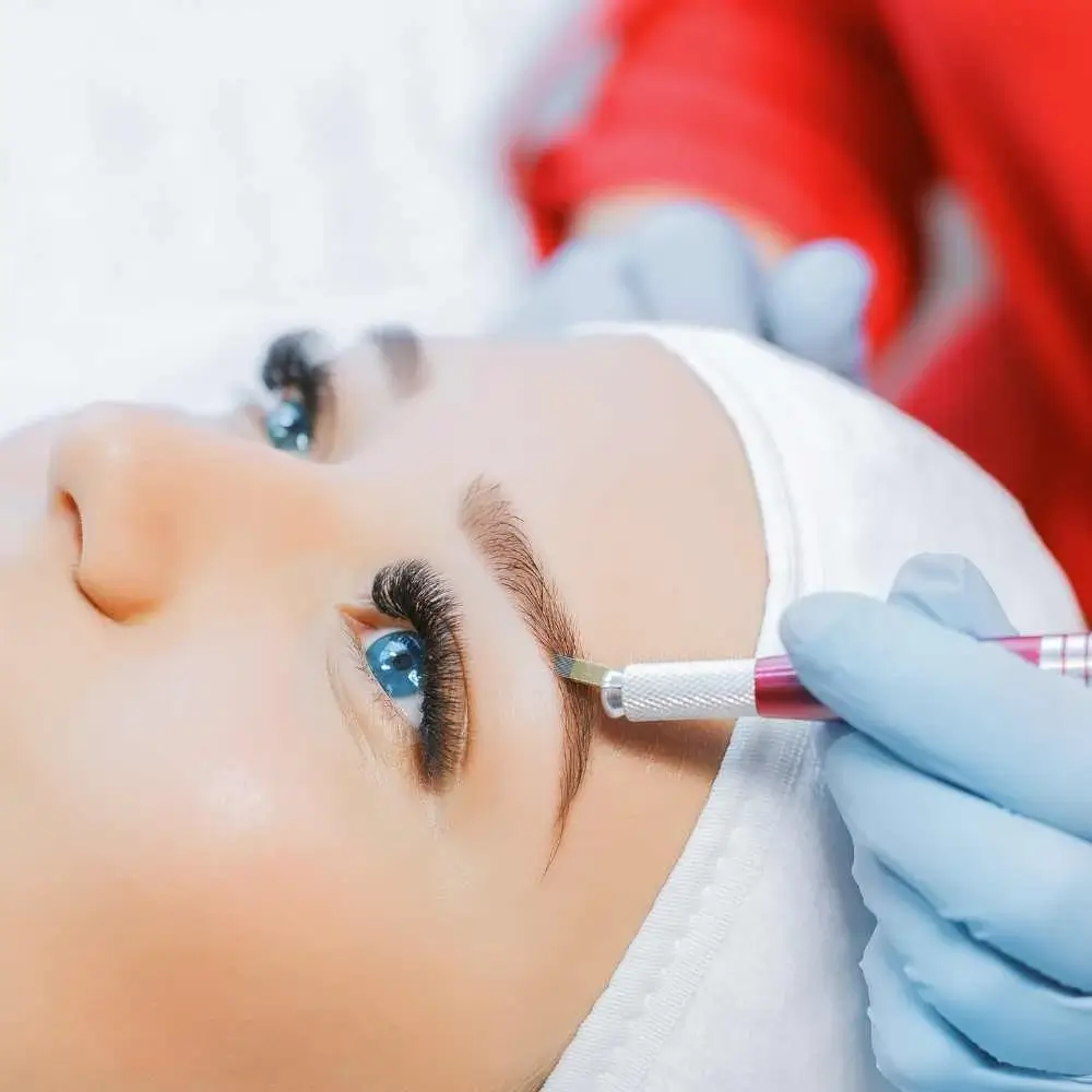 woman with thick lashes having a microblading procedure on her eyebrow