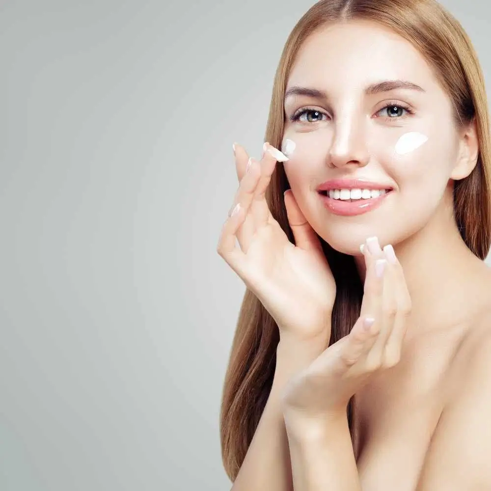 smiling woman applying cream on her face