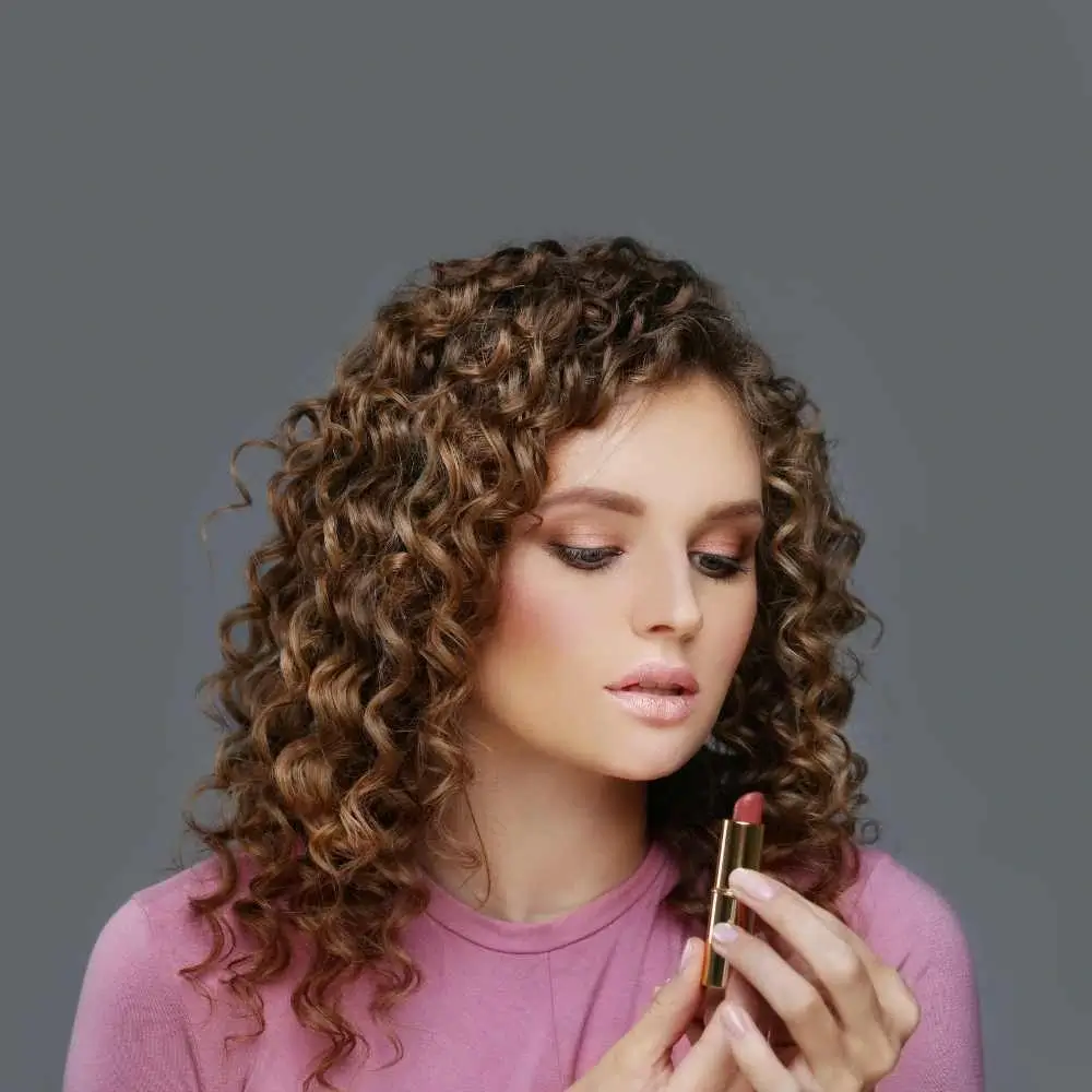 curly woman holding and looking at her lipstick