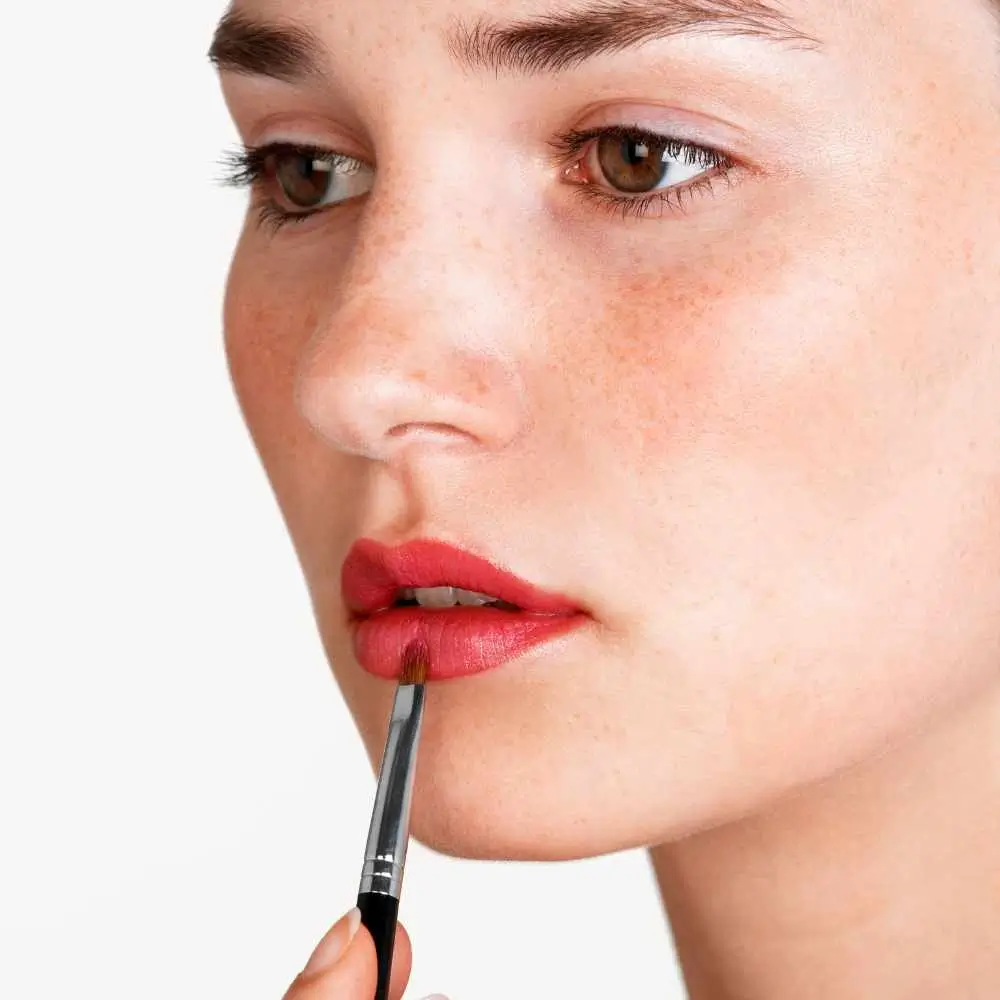 close-up shot of woman's face applying lipstick using a lip brush