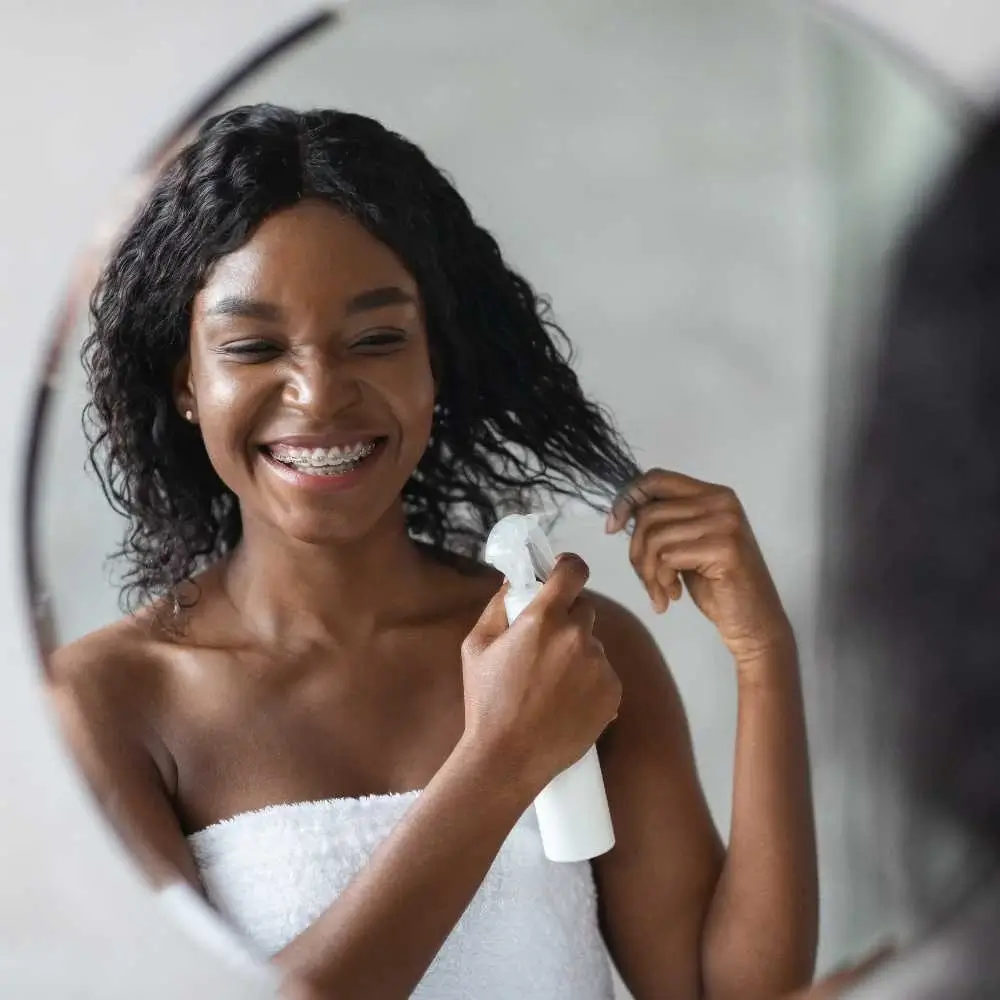 black woman spraying leave in conditioner on her hair in front of the mirror
