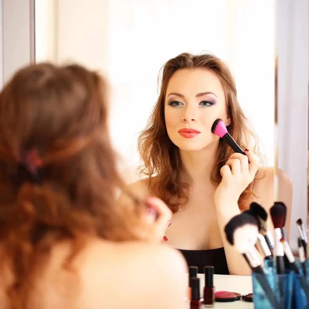 woman applying makeup in front of a mirror