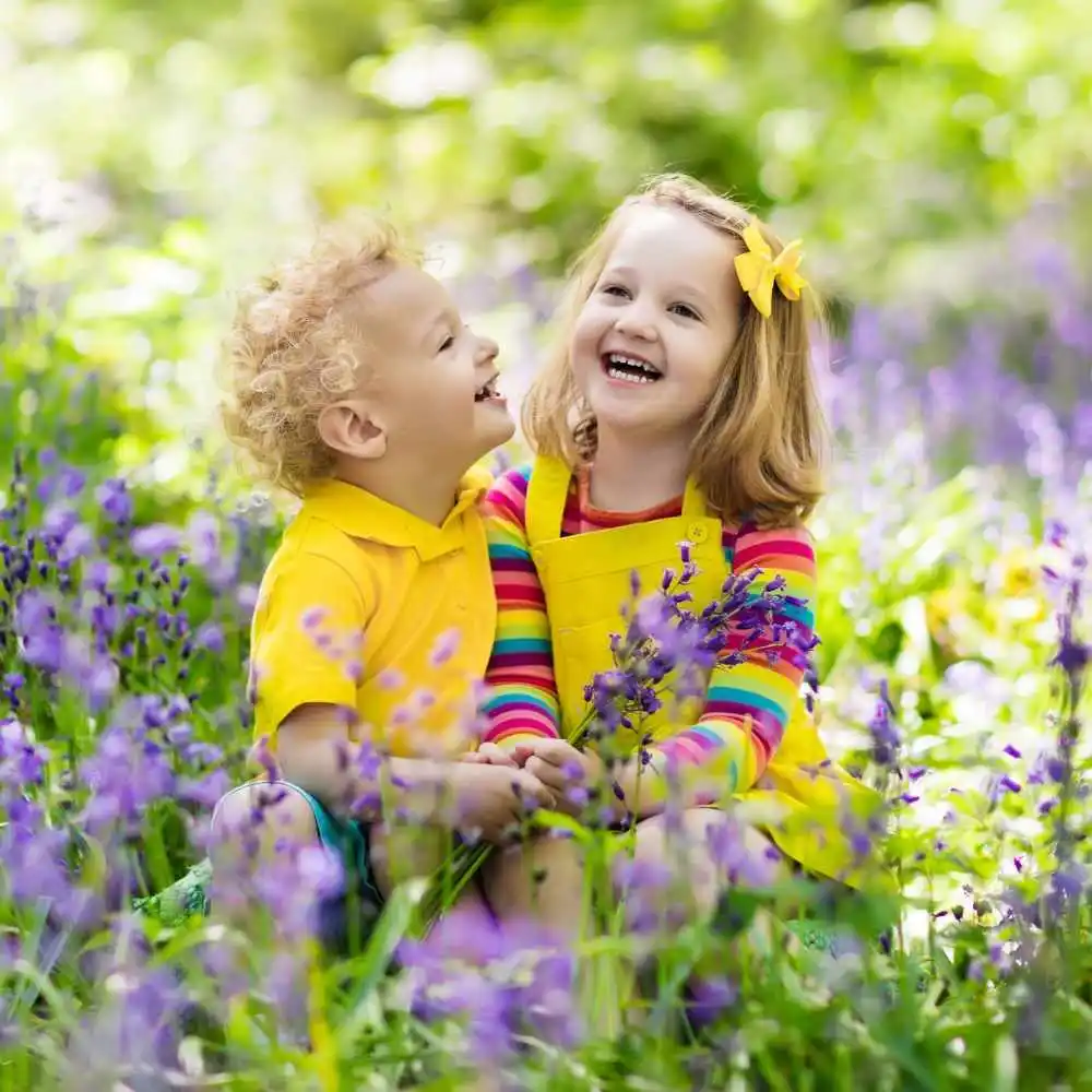 little boy and girl sitting and laughing in the field of flowers