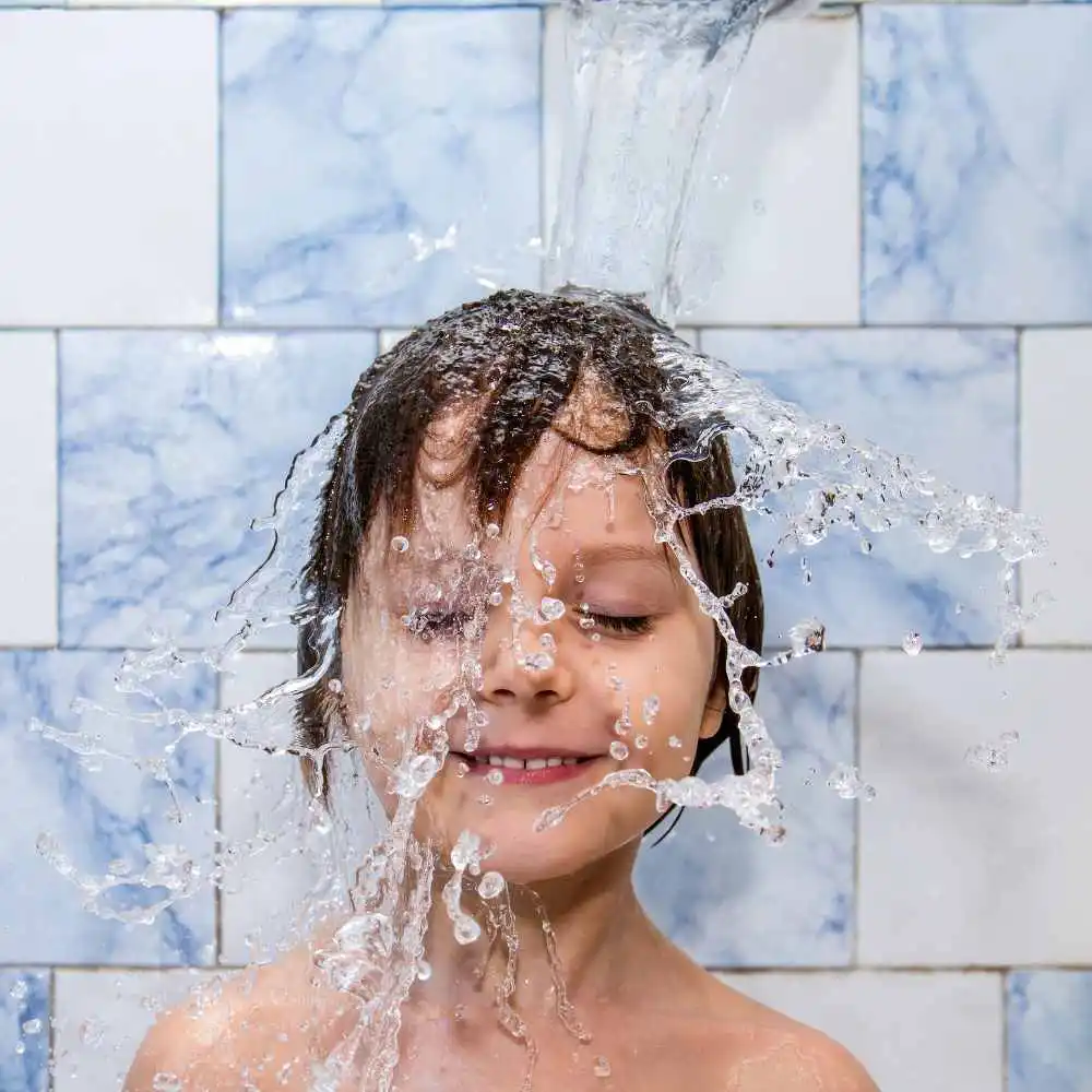 little boy taking a shower with water splashing on his face and head