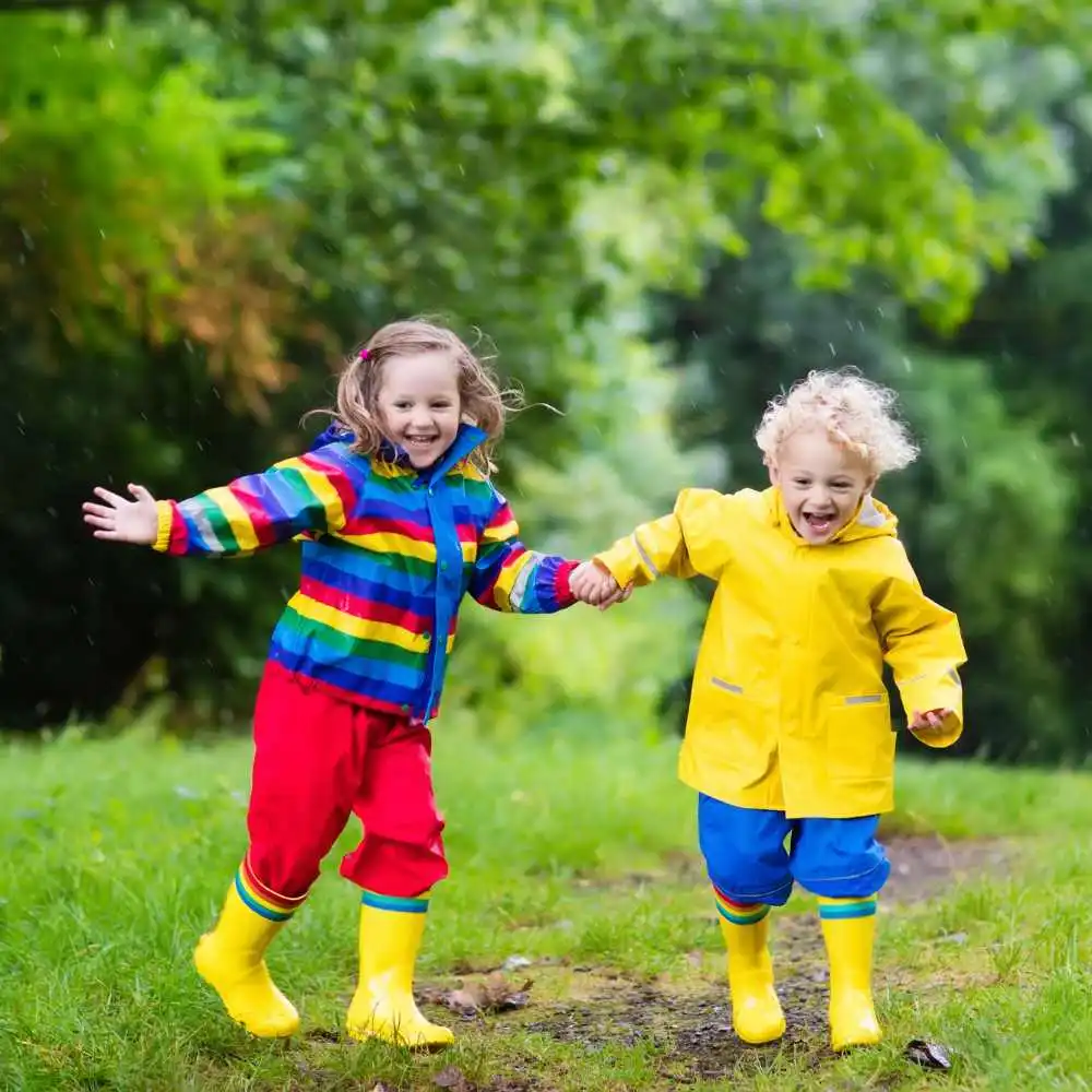 little girl and boy with yellow boots and colorful jackets playing under the rain