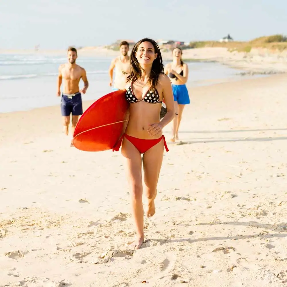 woman running while holding a red surfboard with two men and one woman behind her