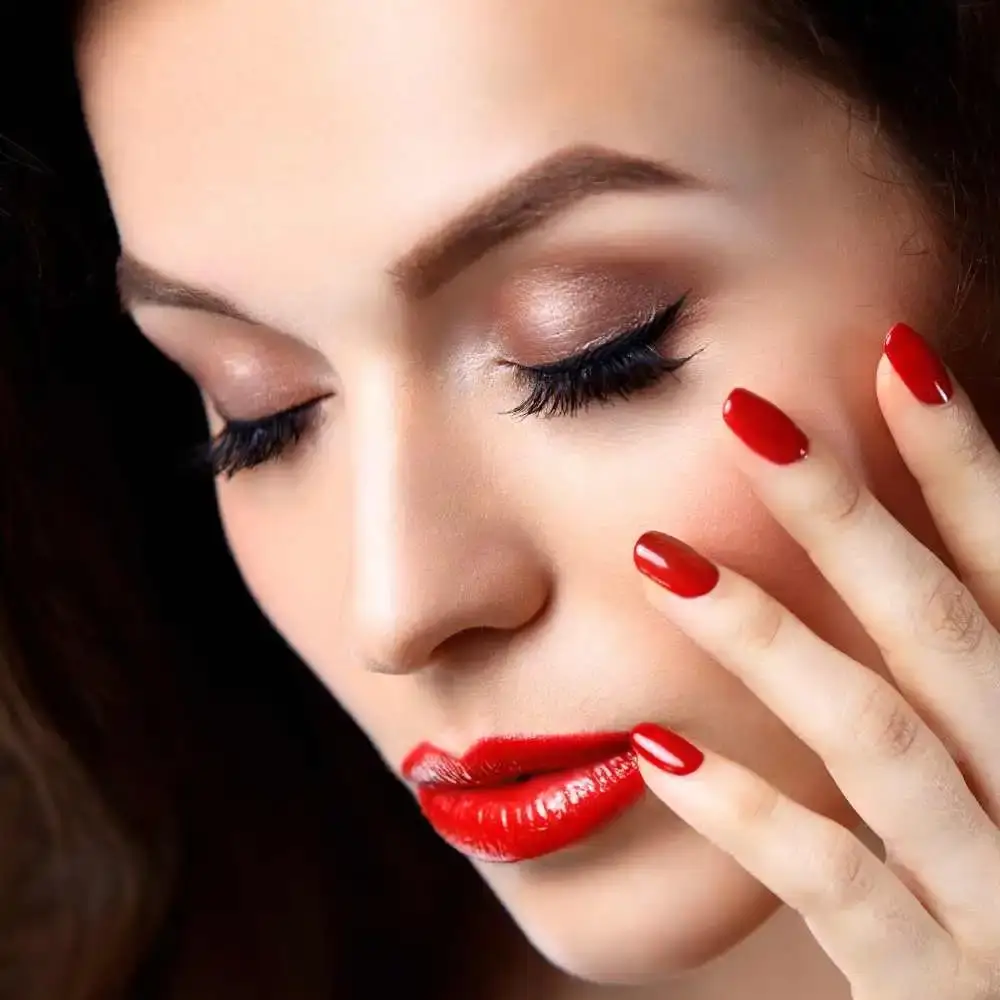 close-up shot of a woman's face with red lipstick and her hands with red nail polish