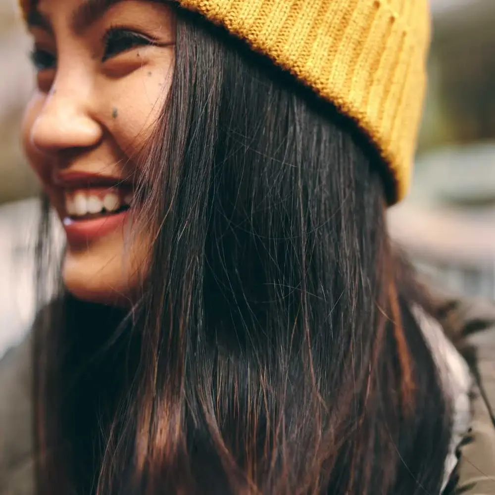 smiling asian woman with black hair and wearing a yellow beanie