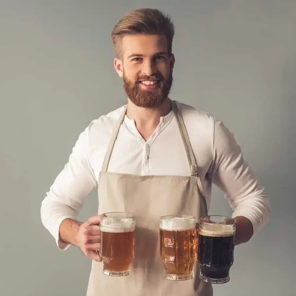 man wearing an apron holding glasses of beer