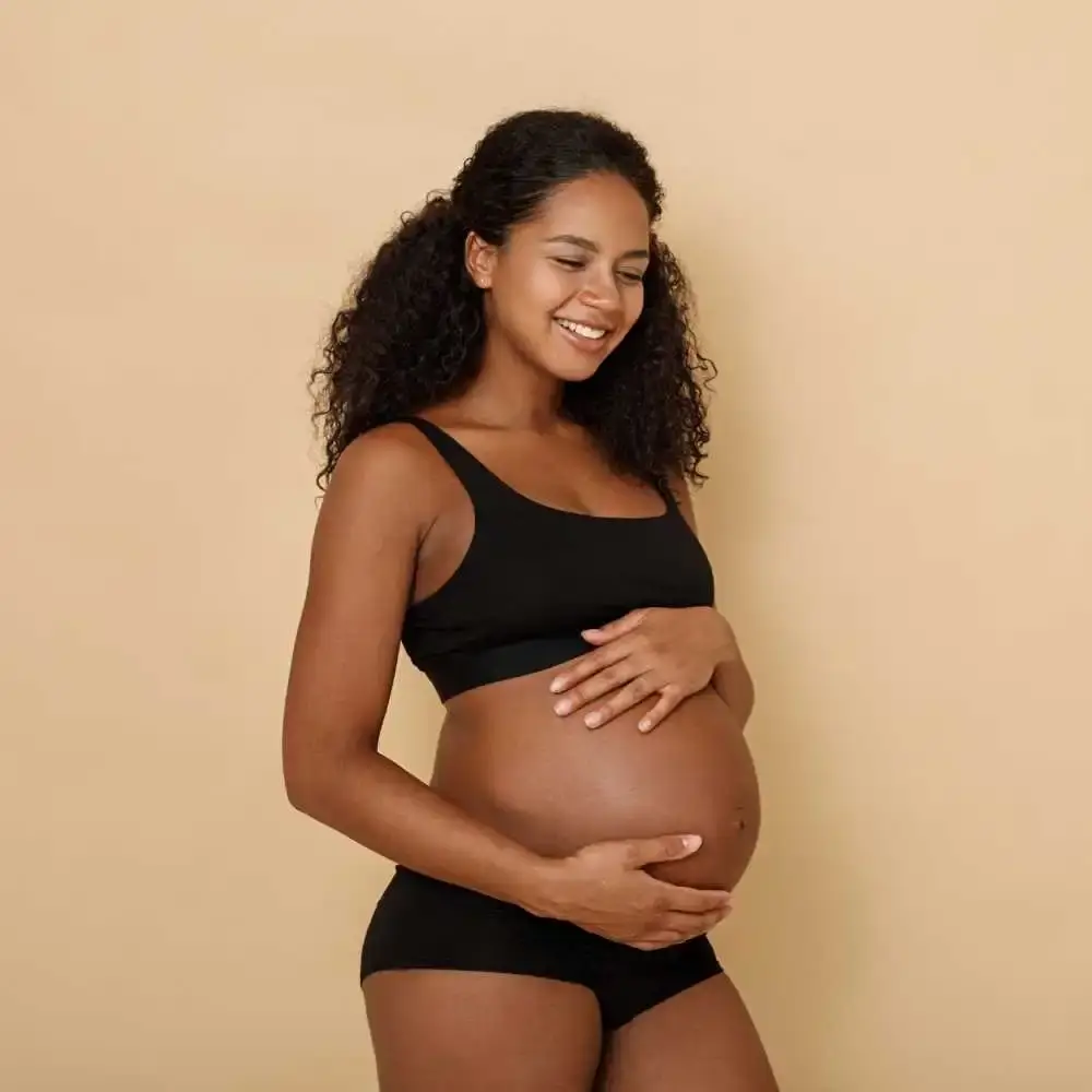 pregnant woman with curly hair smiling while rubbing her belly