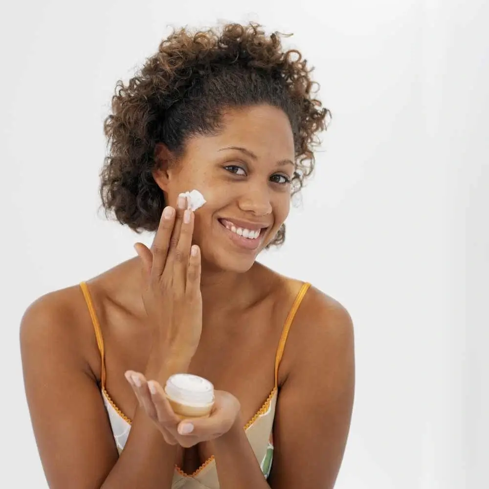 curly woman smiling and applying vitamin c cream on her face
