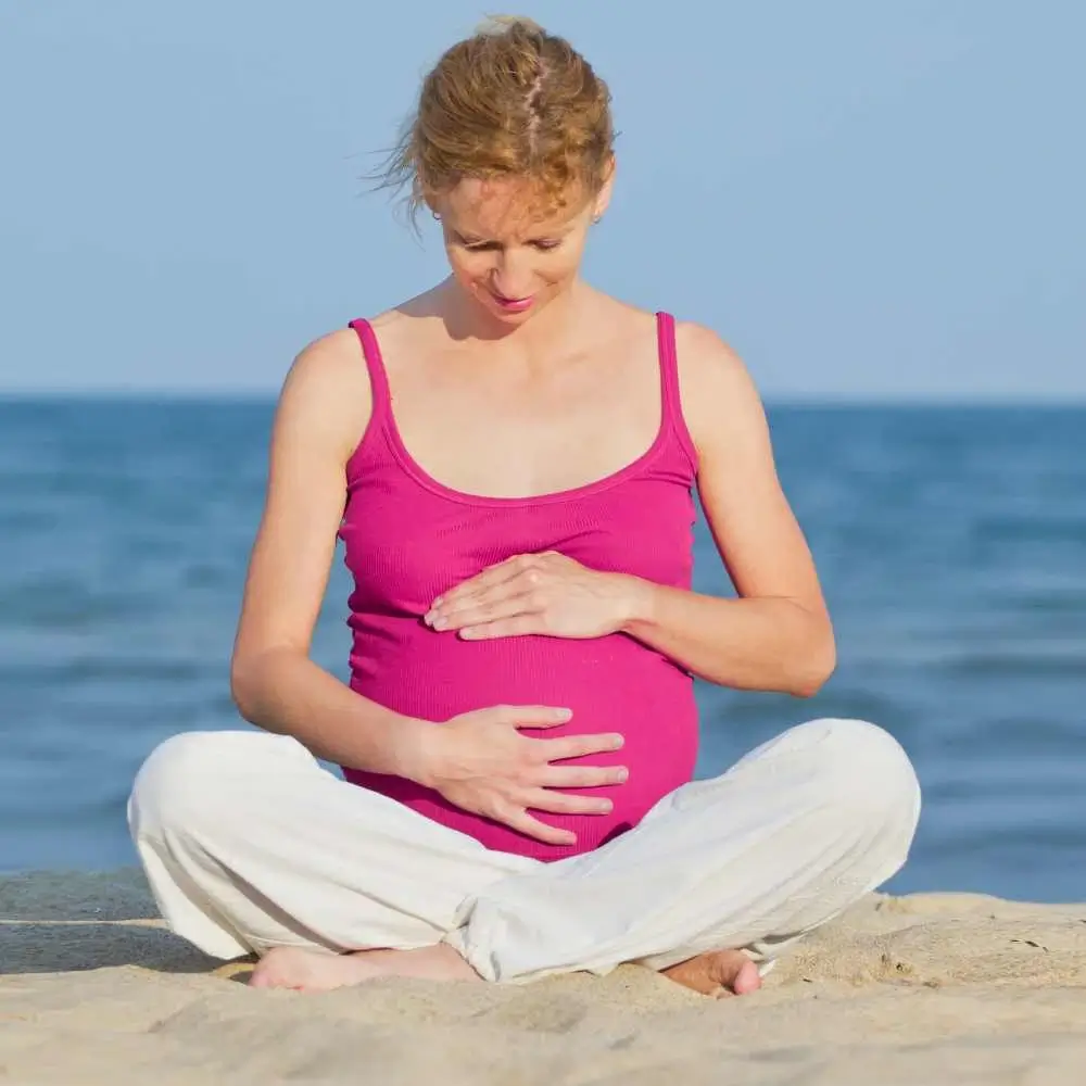 preganant woman sitting on the beach holding her belly
