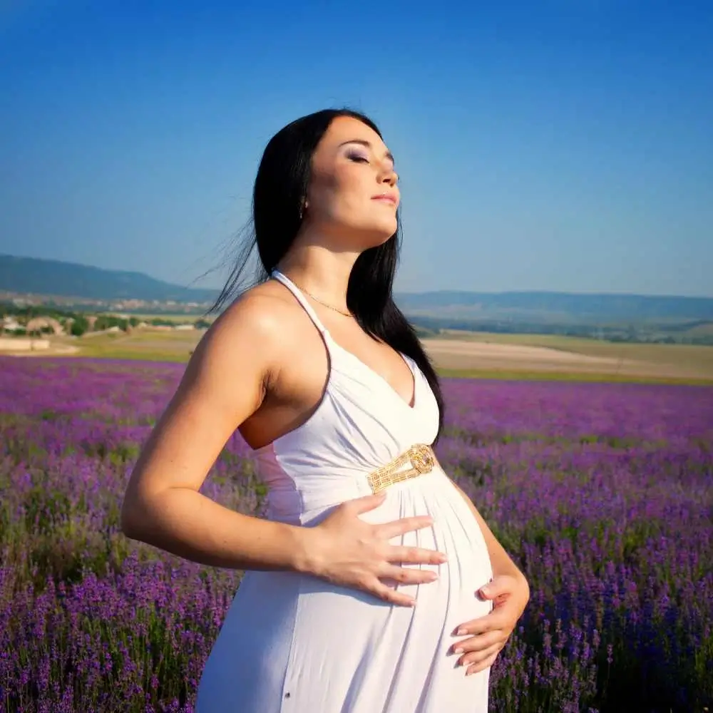 pregnant woman wearing a white dress standing on a lavender field