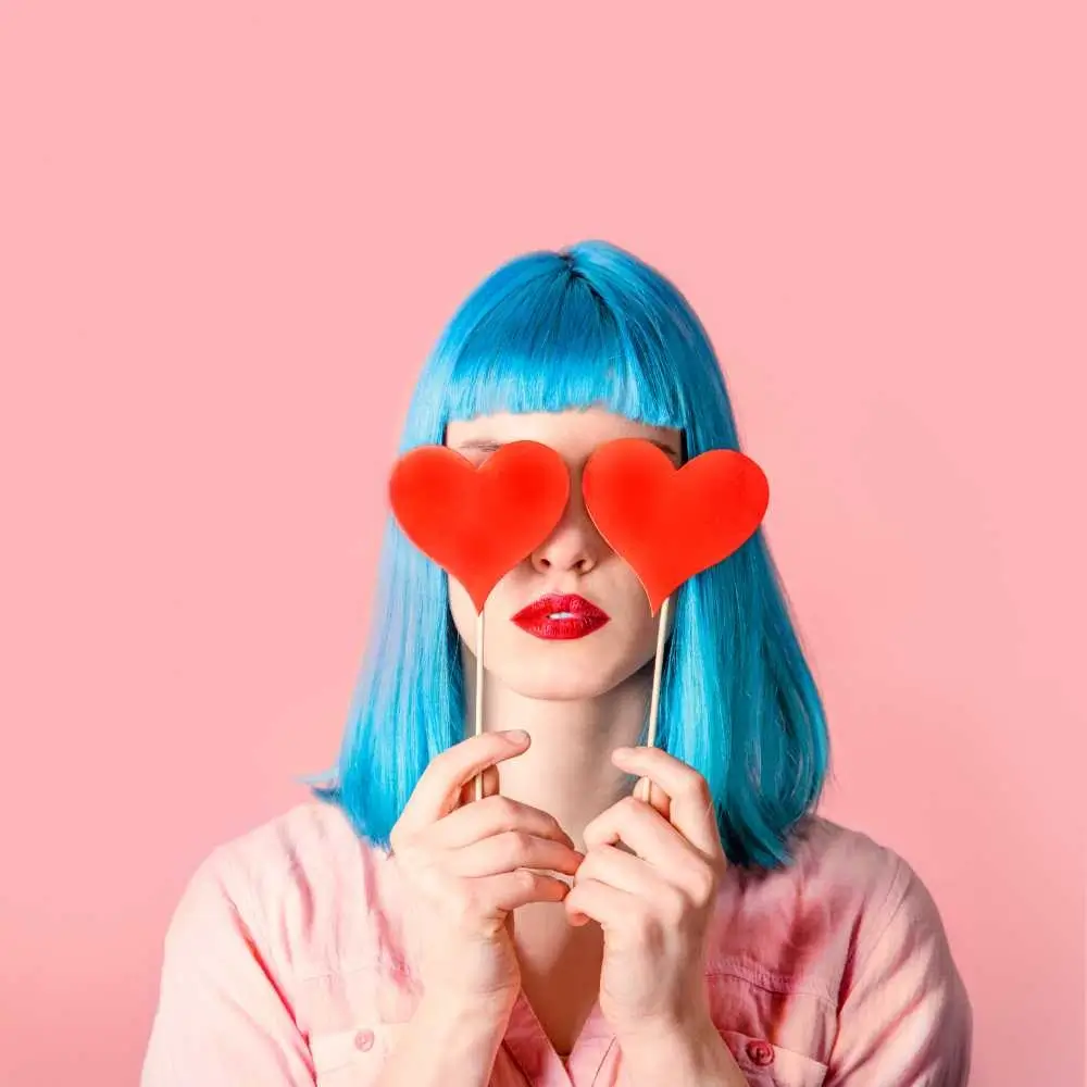 woman with blue hair covering her eyes with red hearts on sticks