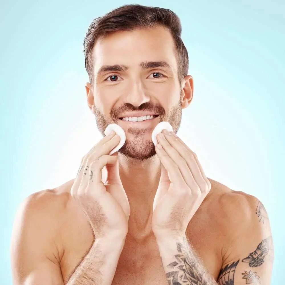 young man with tattoo on his left arm applying toner on her face with cotton pads