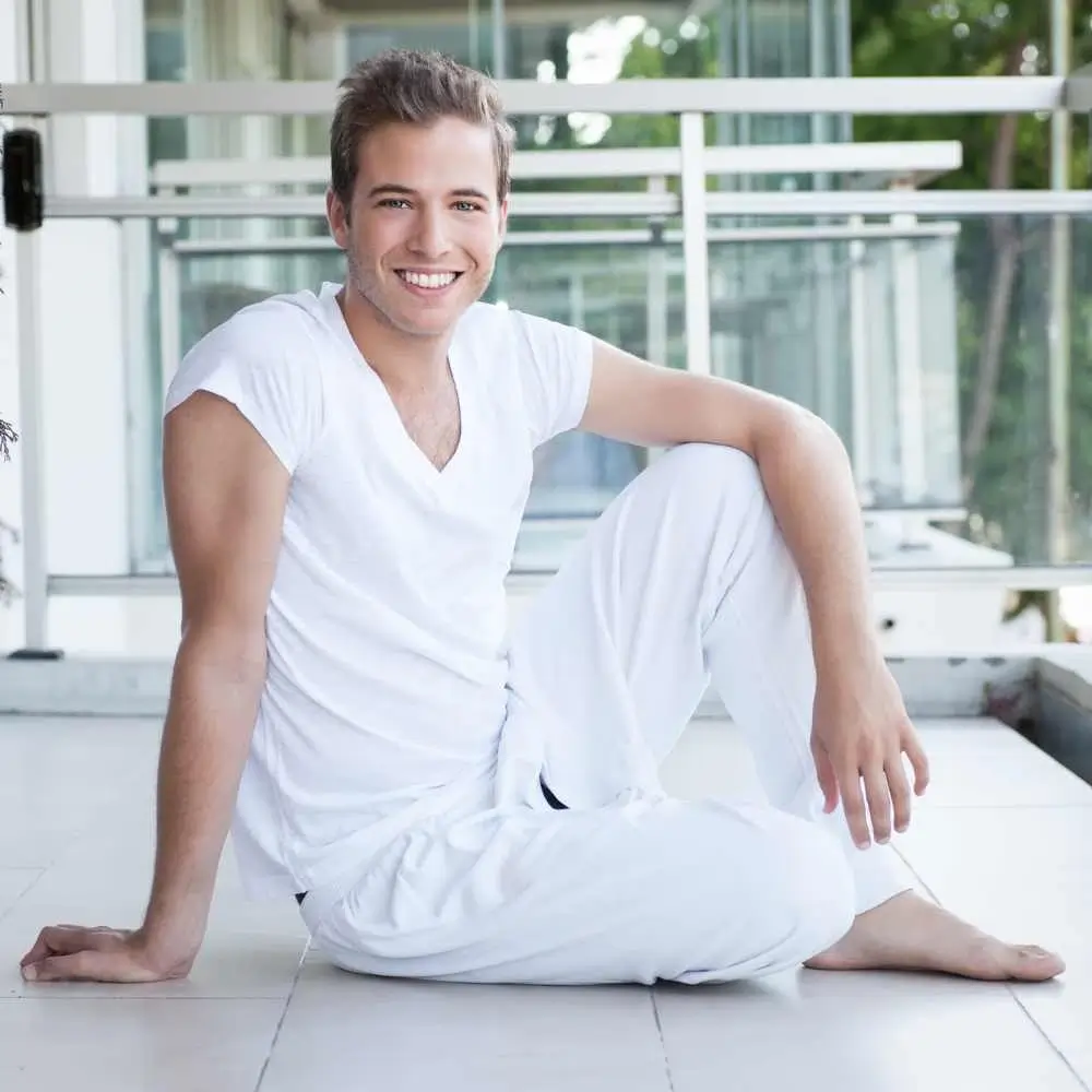 young man dressed in white sitting on the floor and looking at the camera