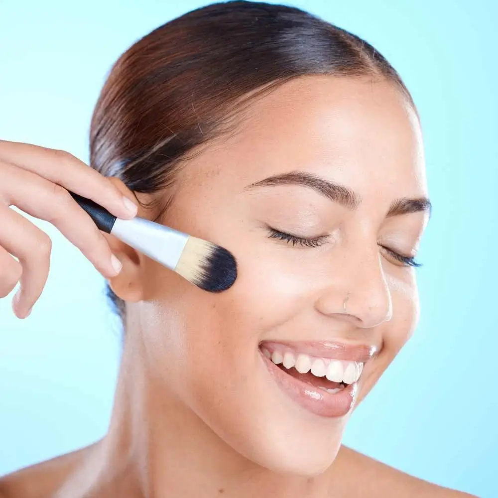 closeup portrait of a smiling woman holding a makeup brush against her cheek