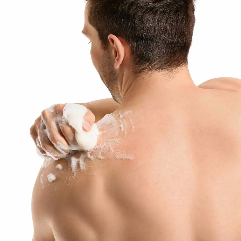 man scrubbing his shoulder with a body scrubber and using body wash