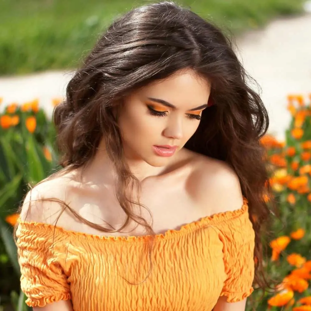 young woman wearing a dark yellow dress with brunette wavy hair