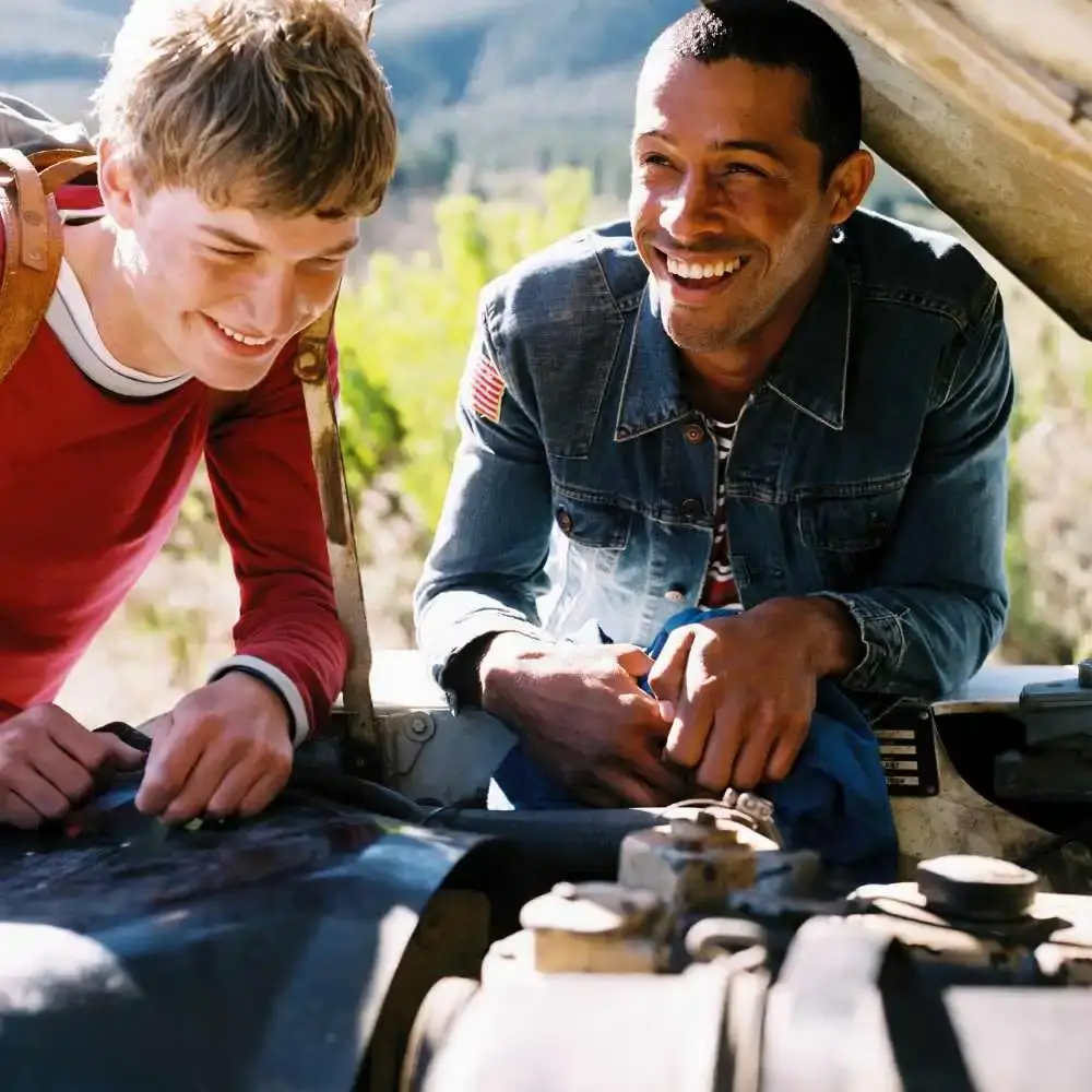 two men smiling and leaning towards the car's engine