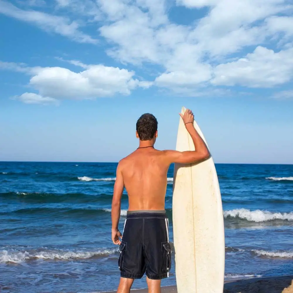 back view of a male surfer holding a surfboard on the beach