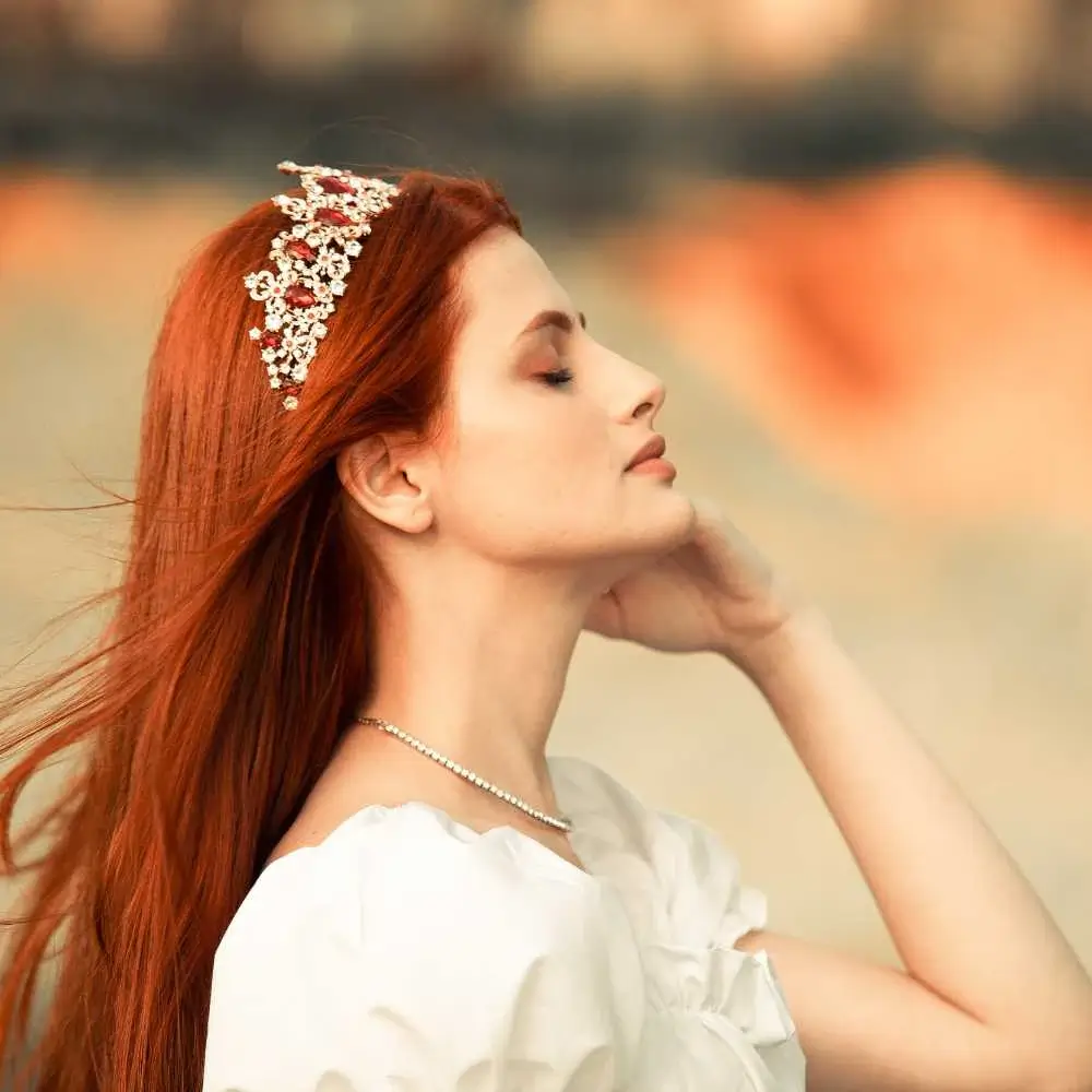 side view portrait of a young redhead woman wearing a white dress and a tiara