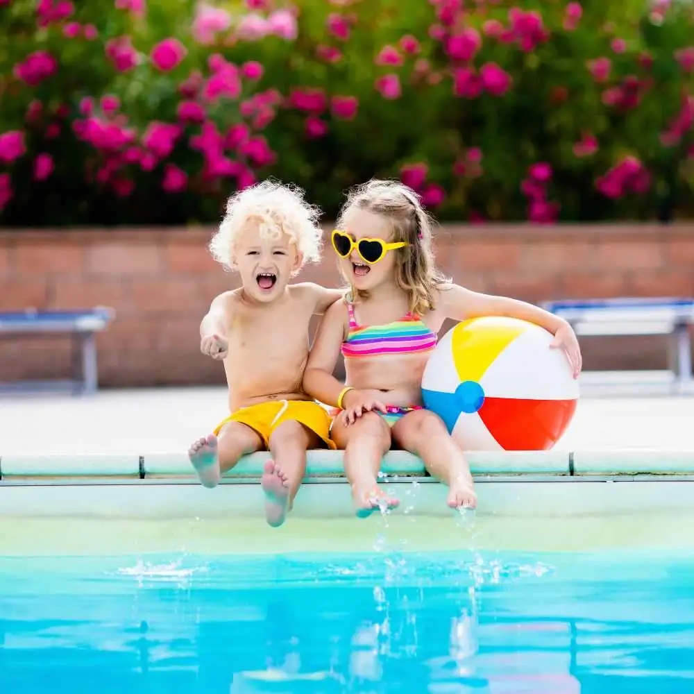 A young boy and a girl sitting by the pool