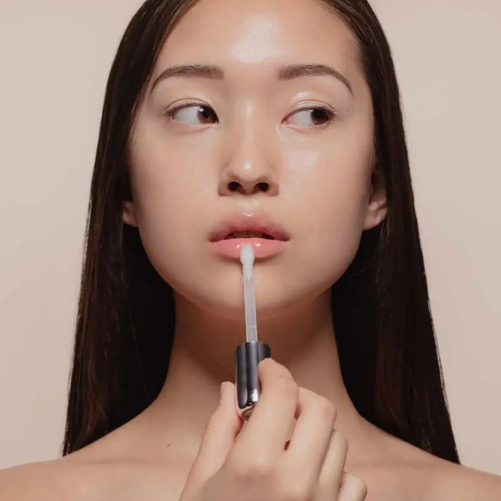 close-up shot of a woman with long black hair applying clear lip gloss