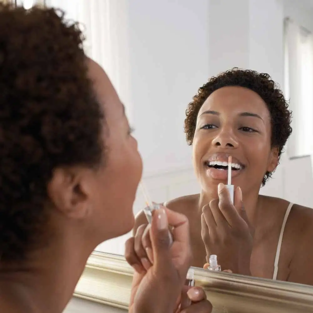 a woman applying clear lip gloss in front of the mirror