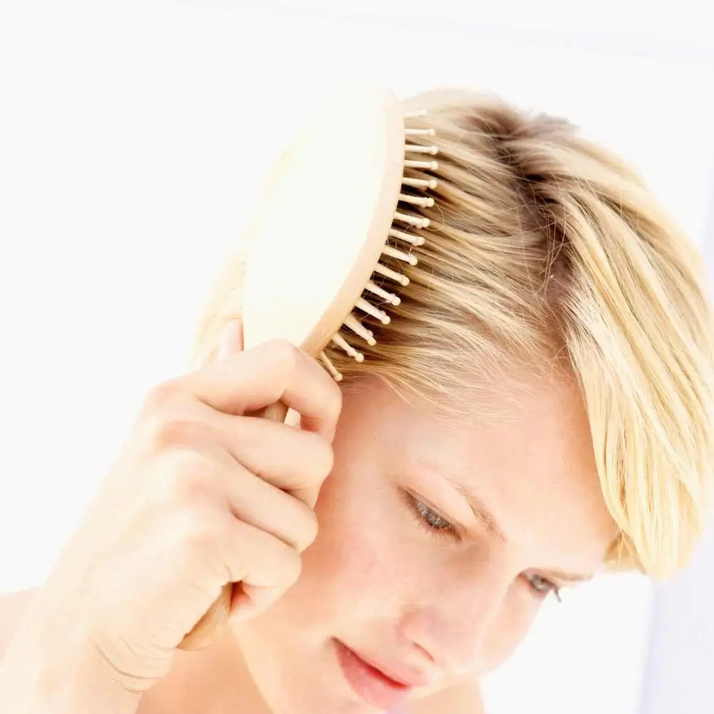 young woman combing her blonde short hair with a wooden hairbrush