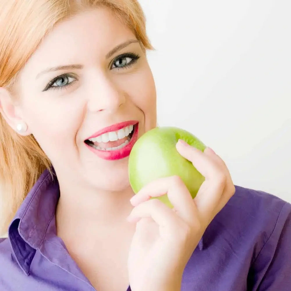 smiling portrait of a woman with beautiful eyes while holding green apple