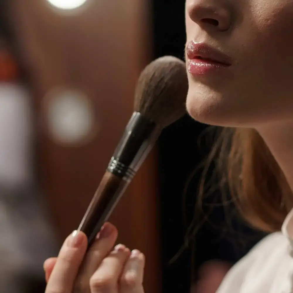 Hand holding a brush applying the best blush on fair skin