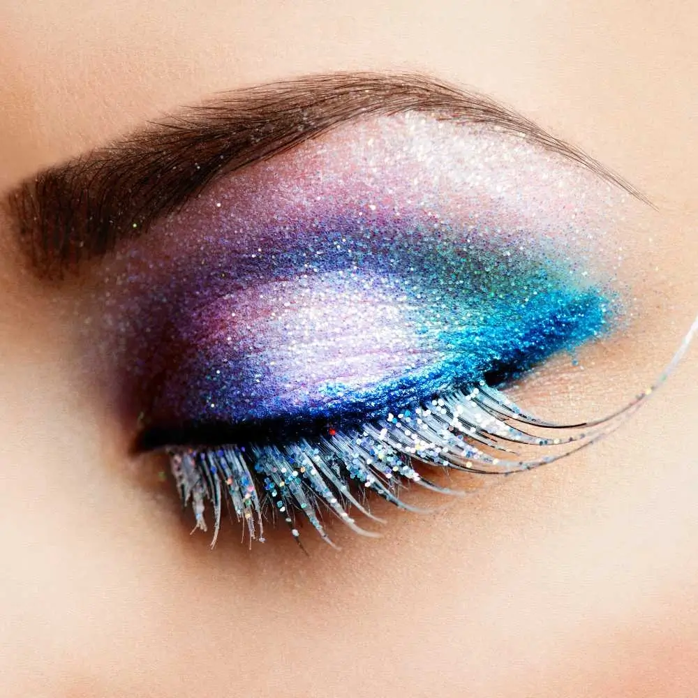 closeup of an eye with rainbow-colored eye makeup and blue glitter eyeliner