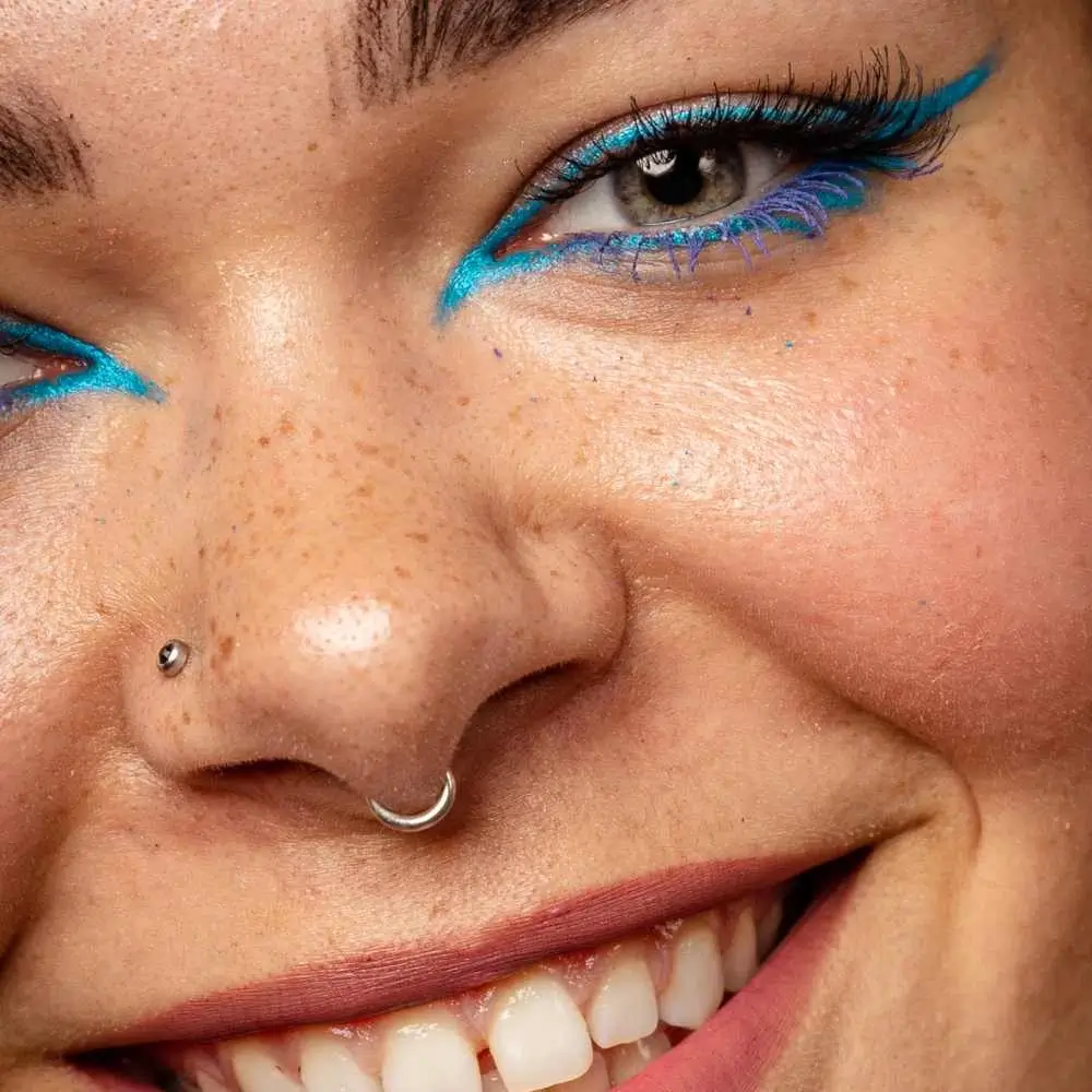 closeup face of a smiling woman with turquoise glitter eyeliner