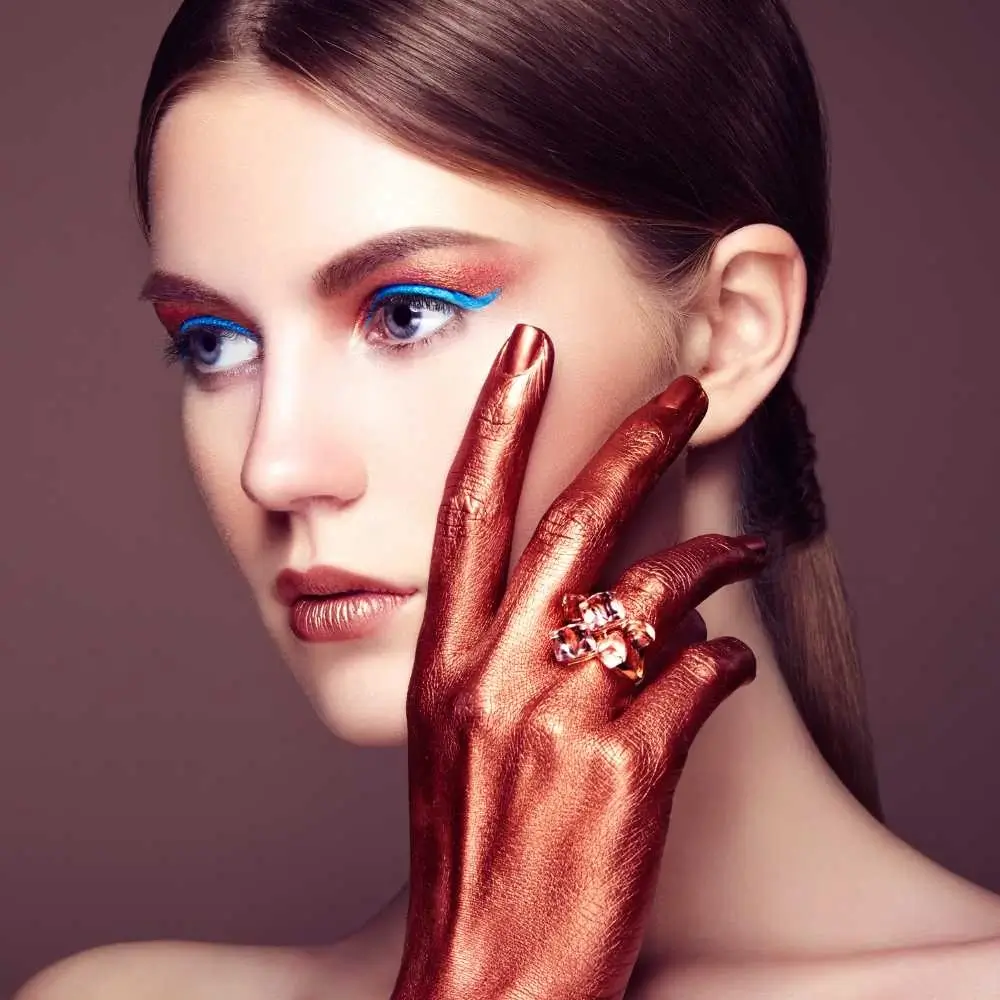 portrait of a beautiful woman with bright blue glitter eyeliner and bronze hand