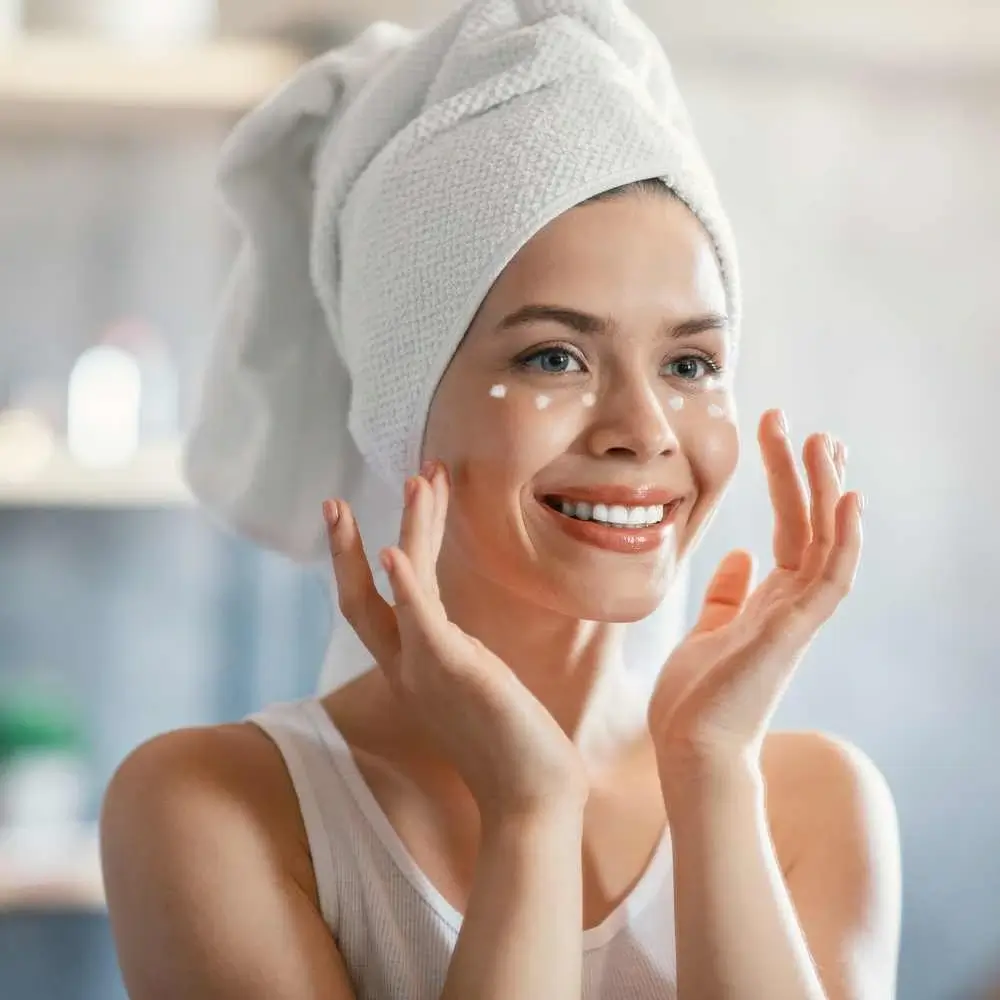 woman with a towel wrapped around her head applying eye cream