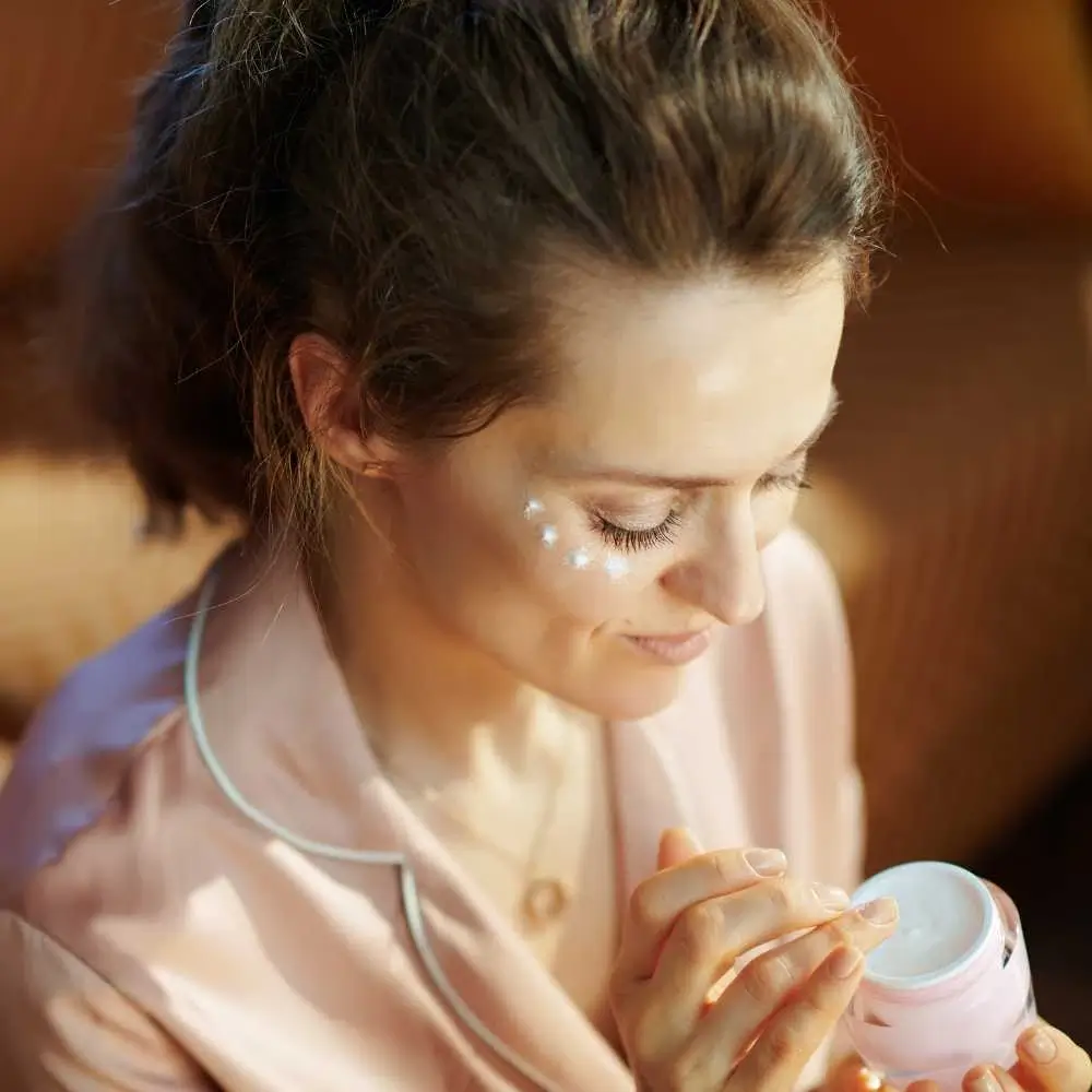 brunette woman in her sleeping wear applying an eye cream