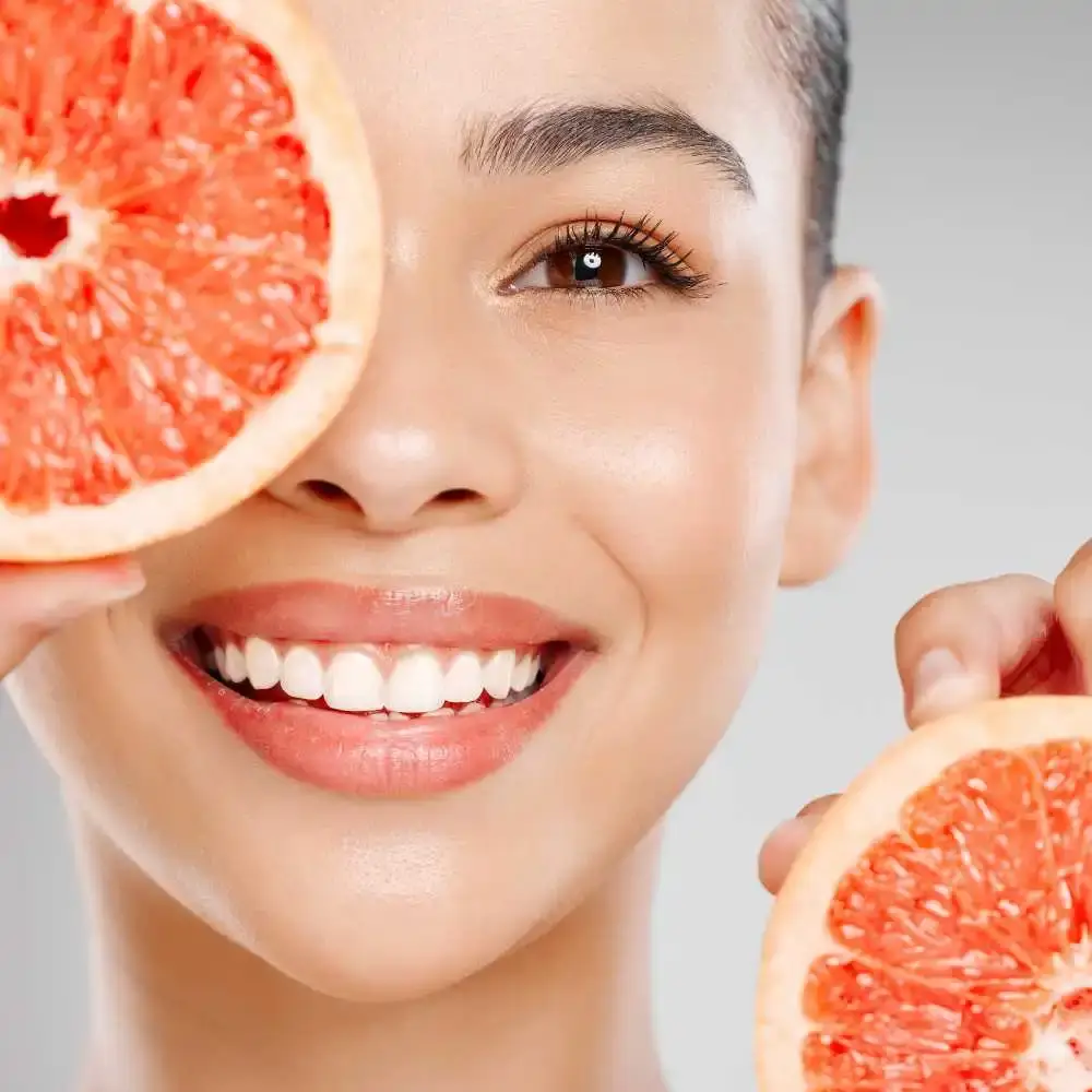 closeup portrait of a woman with radiant skin smiling while holding sliced grapefruit