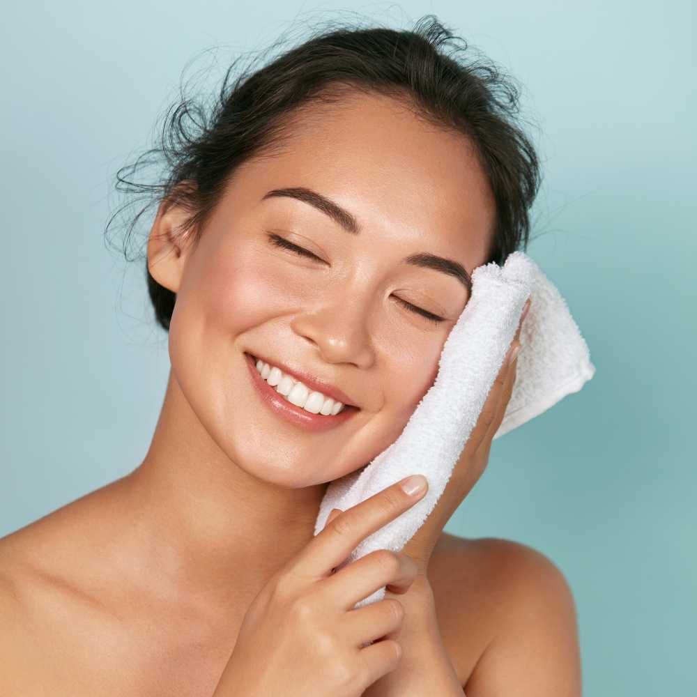 portrait of a smiling asian woman patting her face with a white face towel
