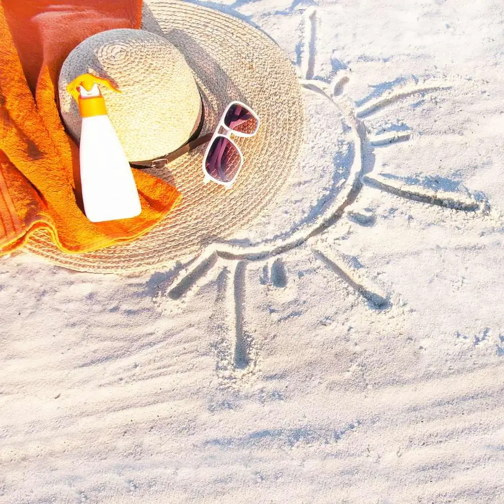 beach hat, sunglasses, beach towel and sunscreen on the sand