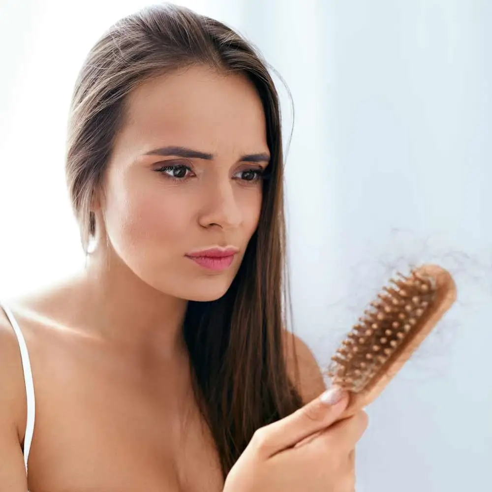 upset woman looking at her hair brush with hair