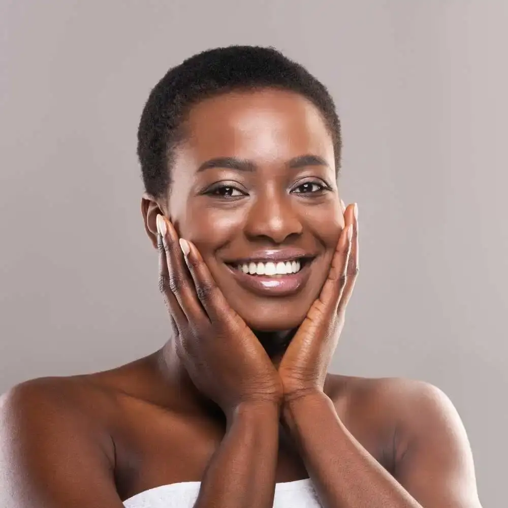 black woman with short hair smiling while touching her face