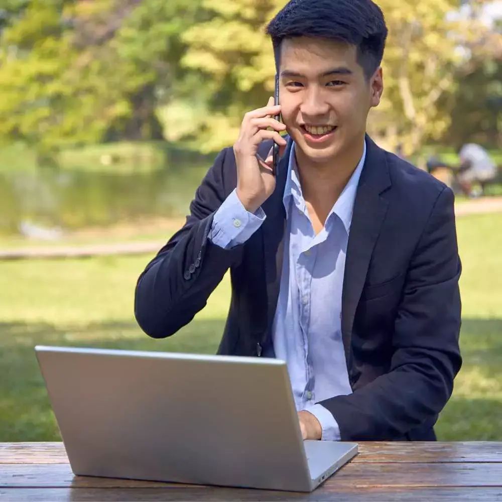 a man smiling and holding a phone over his ear with a laptop in front