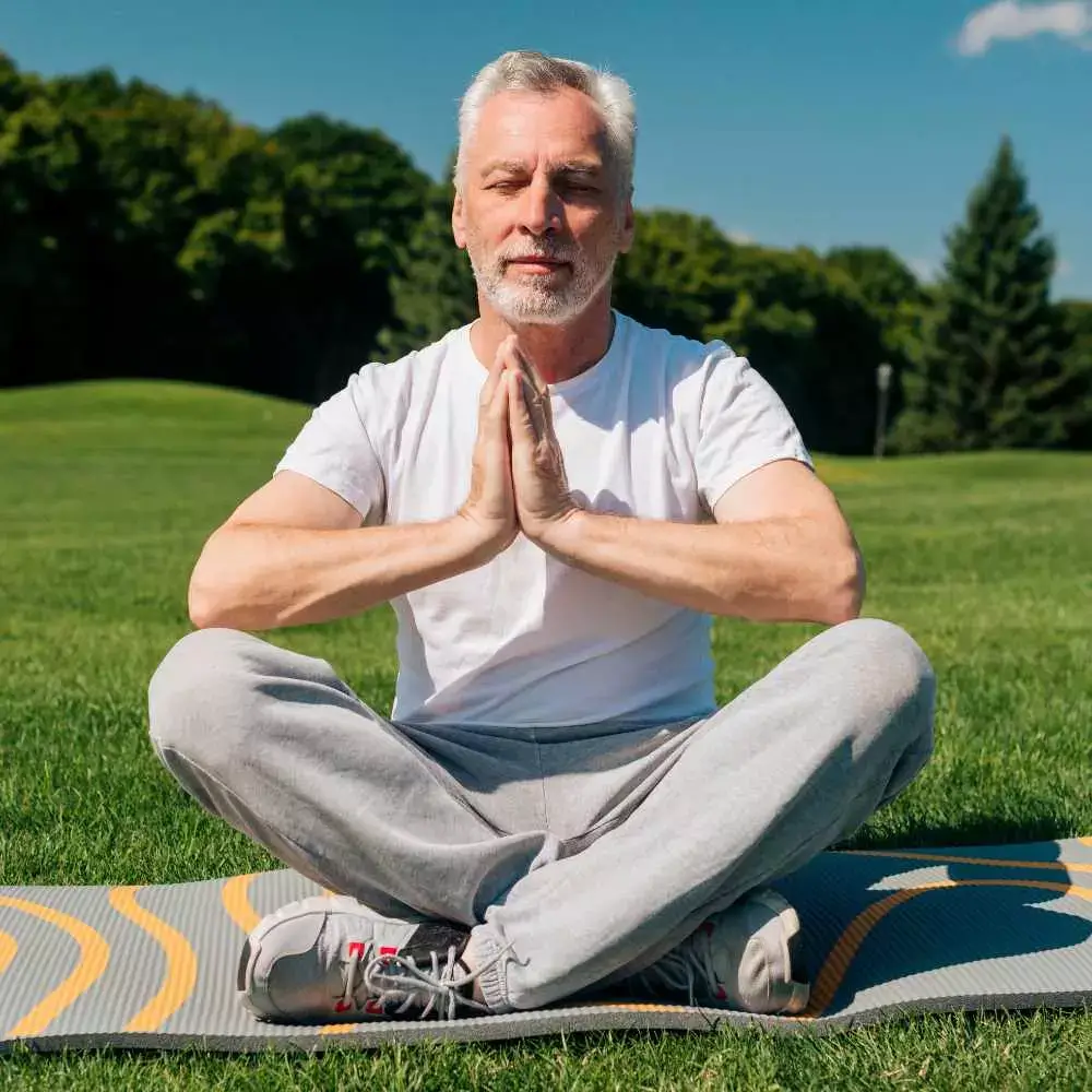 a man wearing a white shirt doing meditation under the sun