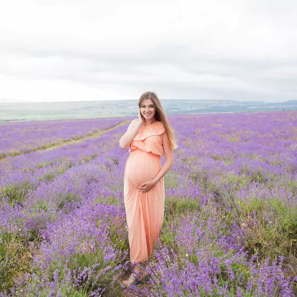 pregnant woman wearing a peach-colored dress stands amidst a lavender field