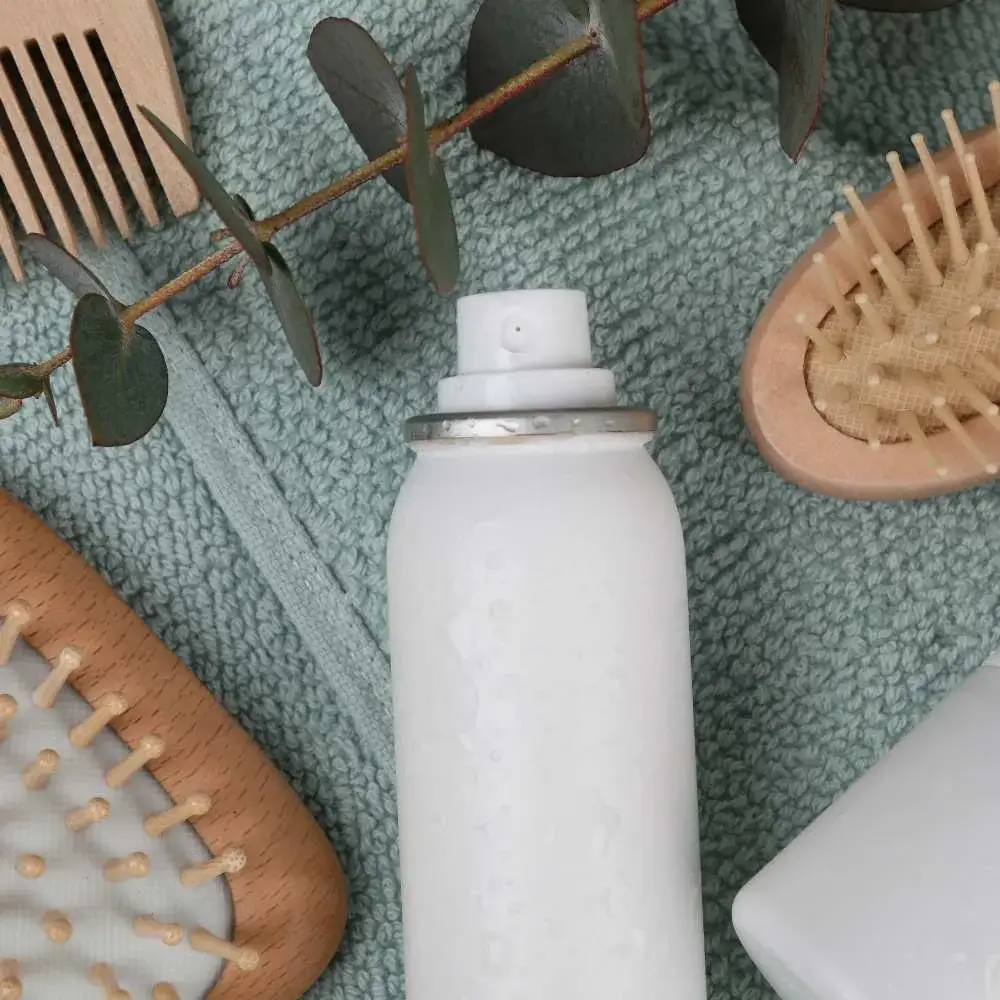 A canister of dry shampoo beside hair brush