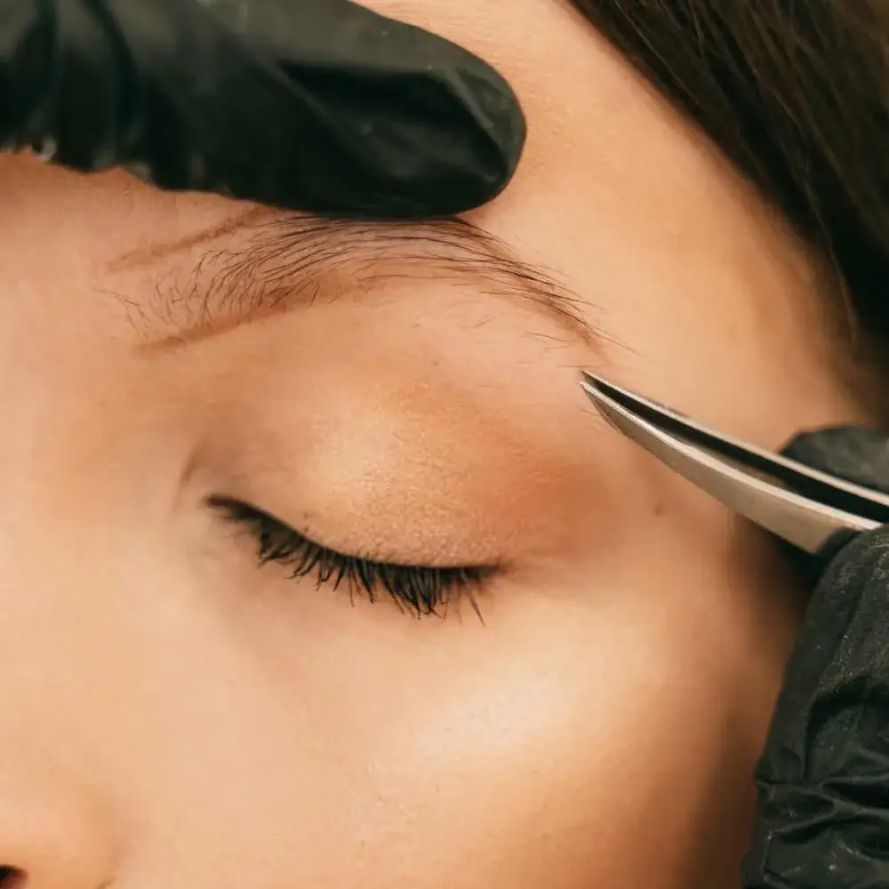 User holding tweezers, poised to groom eyebrows